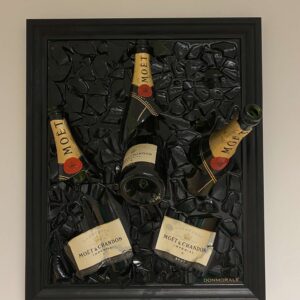 Een zwart omlijst kunstwerk met vier Moët & Chandon champagneflessen ingebed in een gebroken glazen oppervlak.