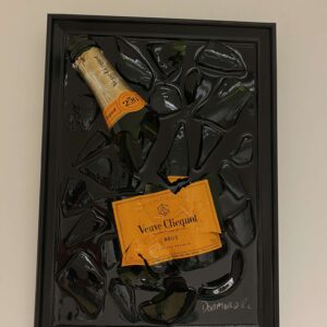 Een zwart omlijst kunstwerk met een Veuve Clicquot champagnefles ingebed in een gebroken glazen oppervlak.